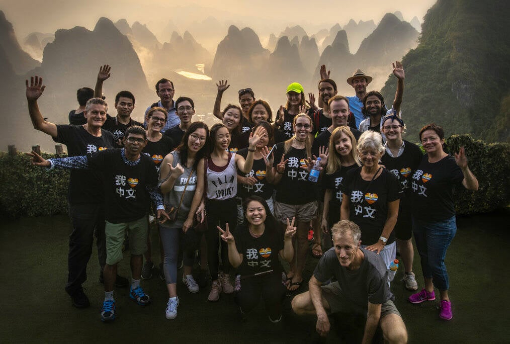 A group of people stand and smile with mountains in the background.
