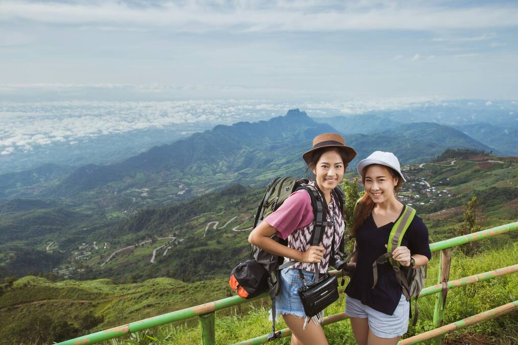 Two women with backpacks stand at the top of a hill.