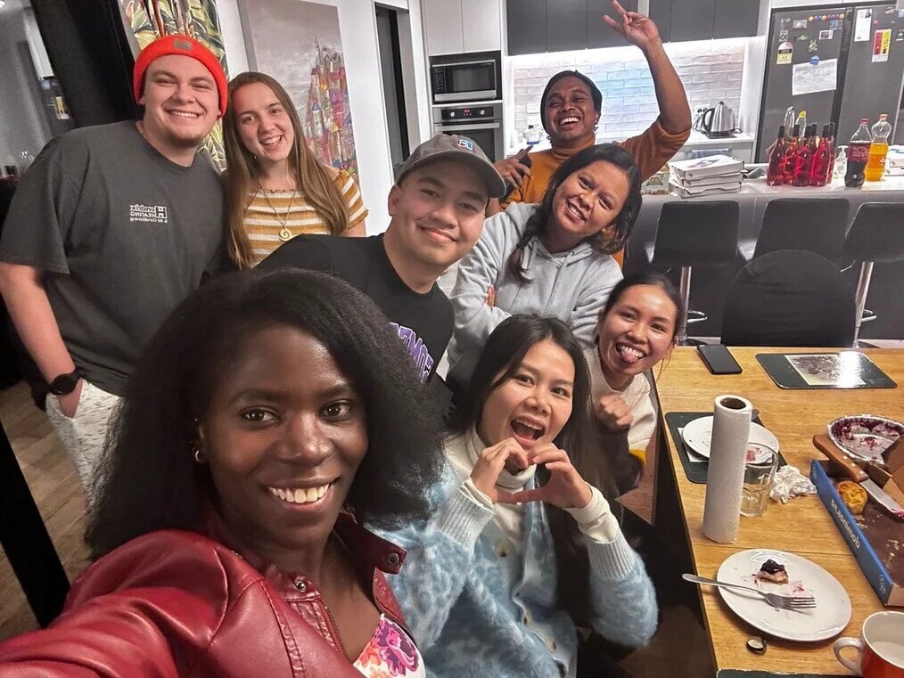 A group of friends around a table smile for the camera.