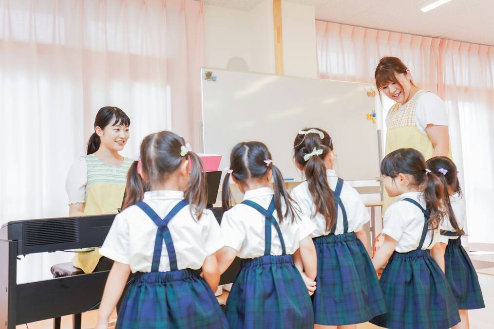 Kids in school uniforms stand around a piano with a teacher.