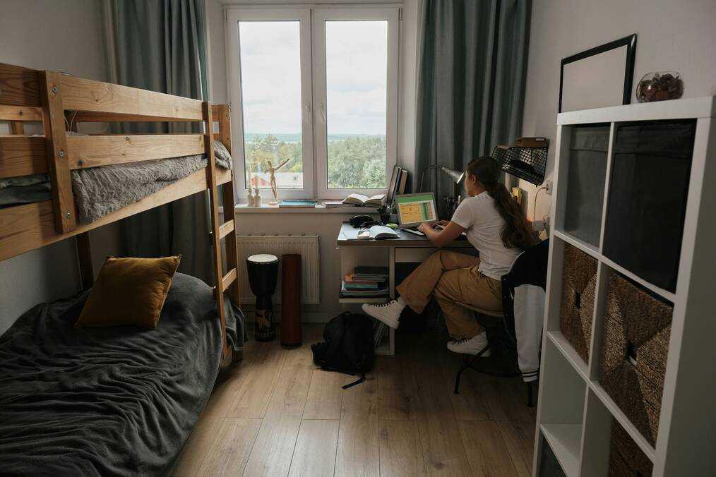 A woman sits at a desk in a student room with bunk beds.