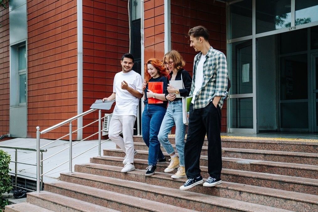 Four students talking and laughing walk down the stairs of a building.