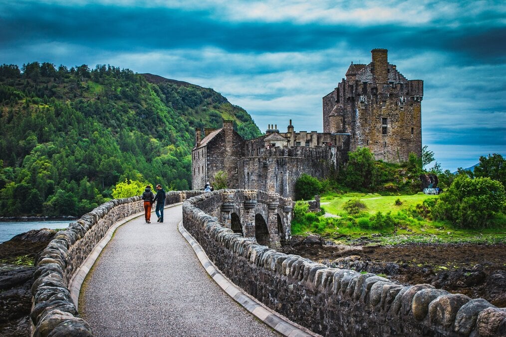 Two people walk over a bridge toward a castle in Scotland.