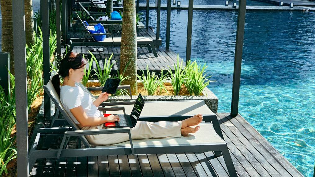 A woman works on a laptop beside a pool.