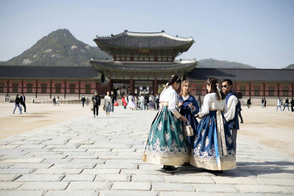 People in traditional Korean dress stand in front of a temple.