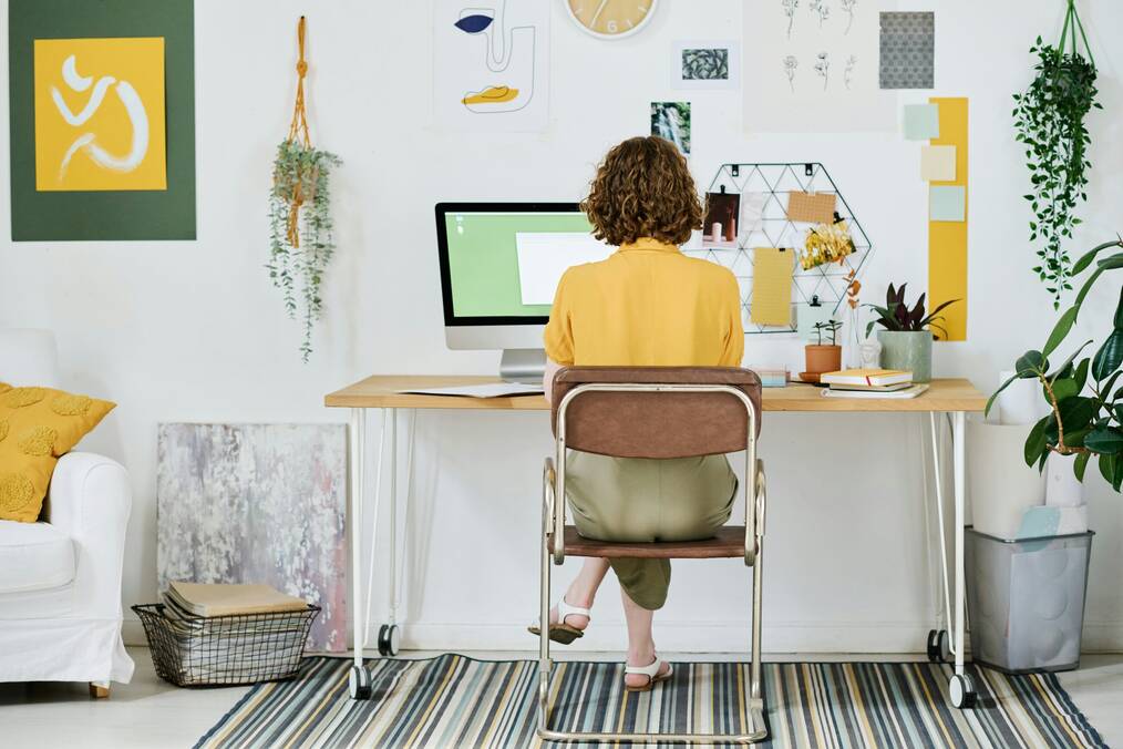 A woman sits at a desktop computer with art on the walls.