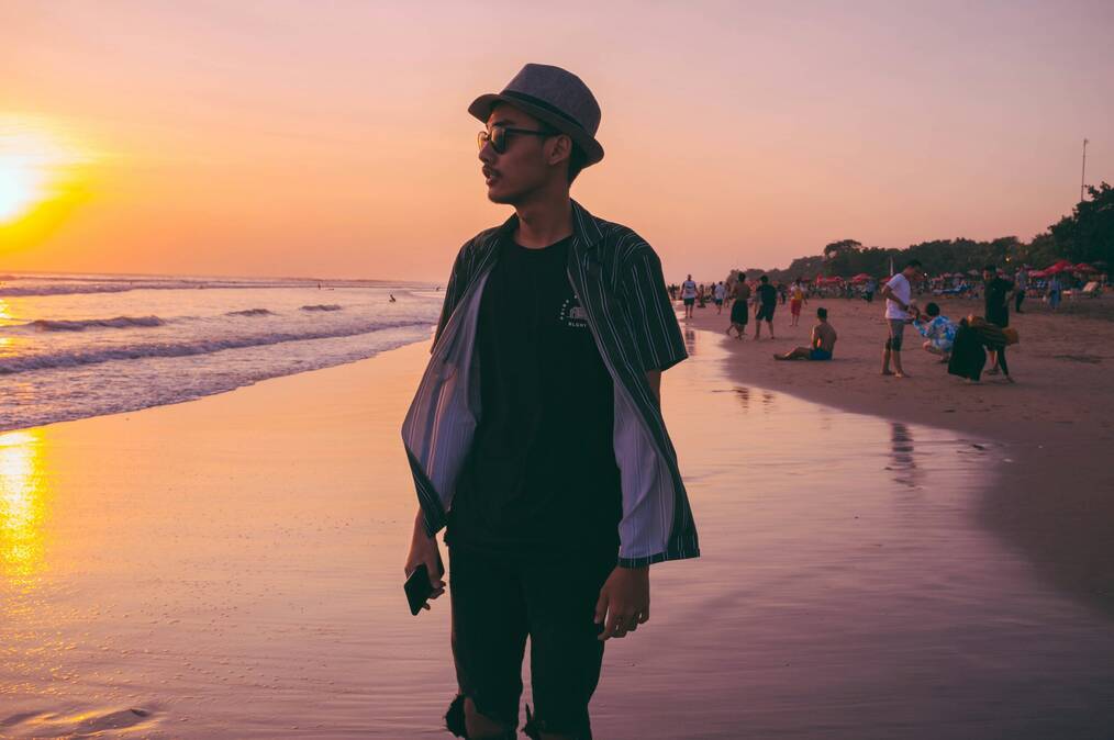 A man walks on a beach in Bali at sunset.