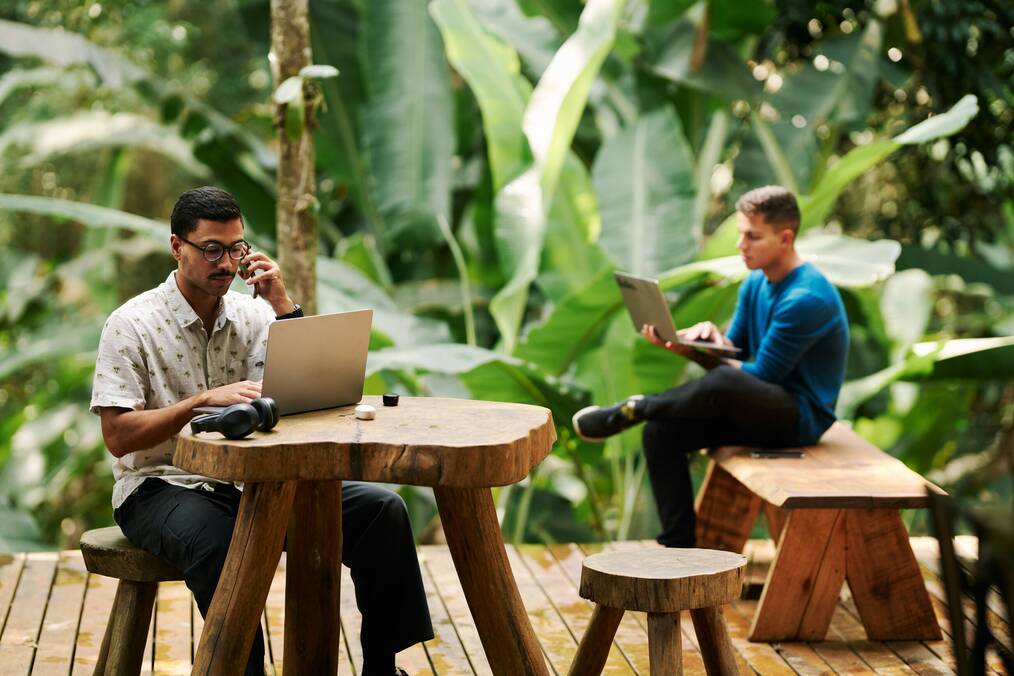 Two men sit outside with laptops.