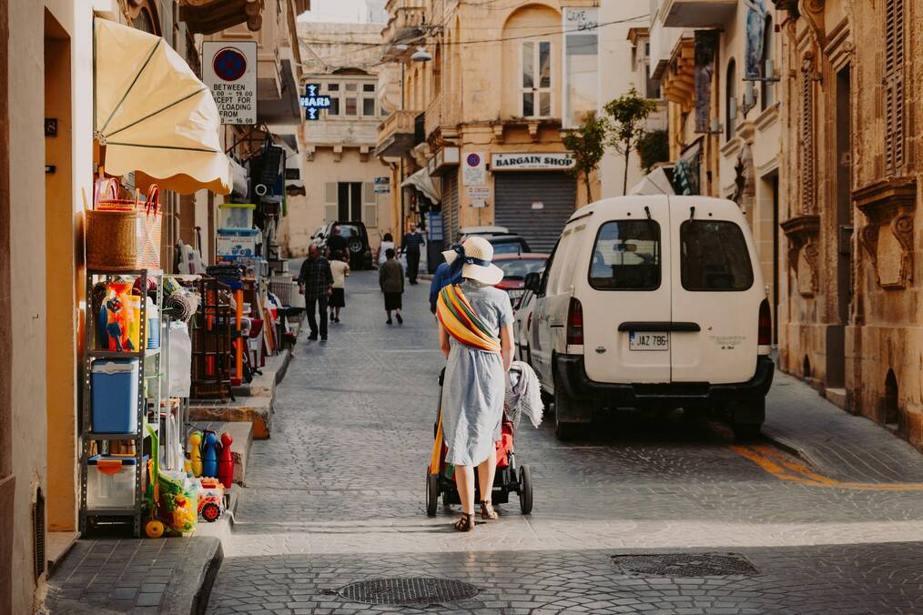 A woman pushing a stroller walks down a street in Malta.