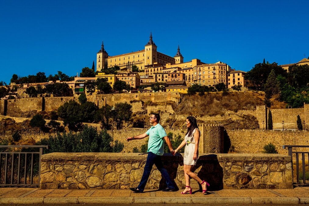 Photo by Alberto Ramírez Sobrino A man and woman hold hands and walk down the street with a castle in the background.