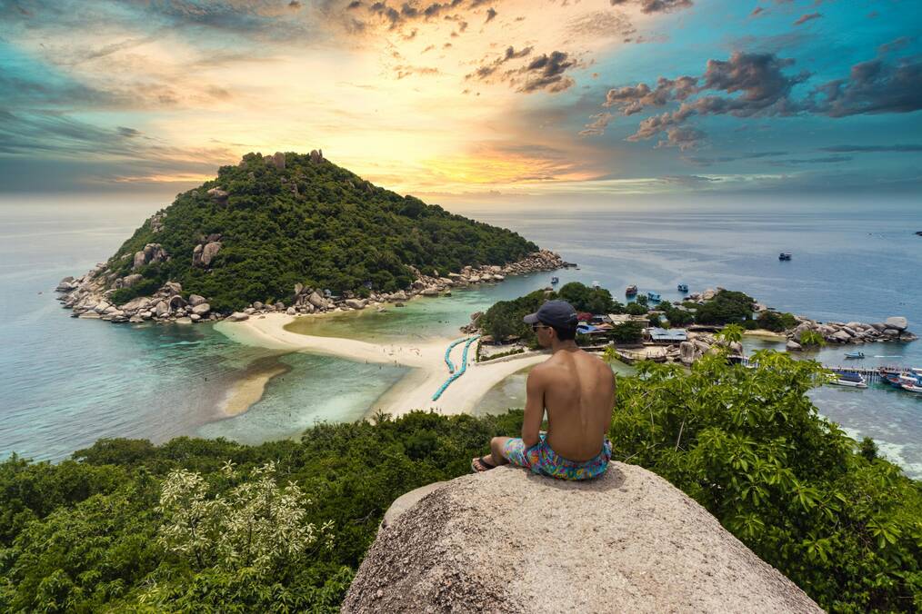 A man sits on a rock overlooking the ocean.