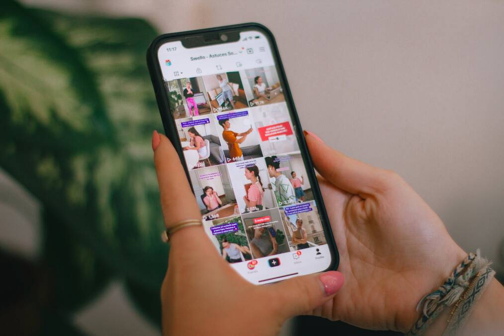 Hands hold a cell phone displaying a TikTok feed.