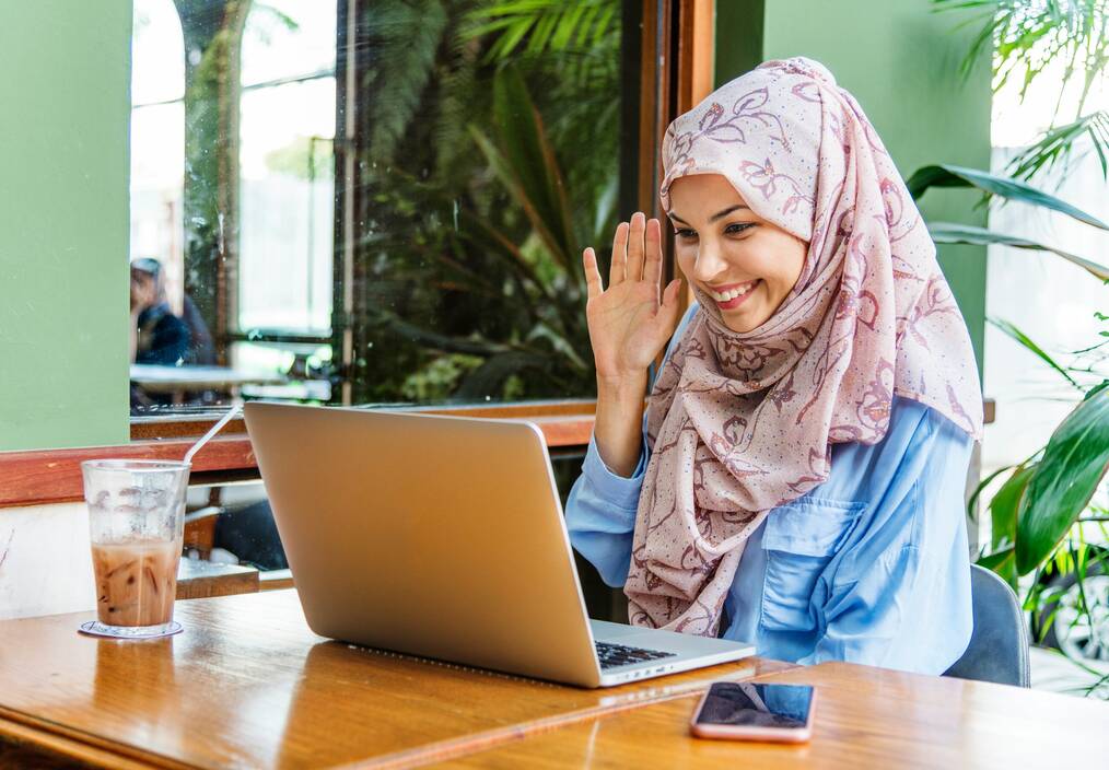 A woman waves at her computer screen during a video call.