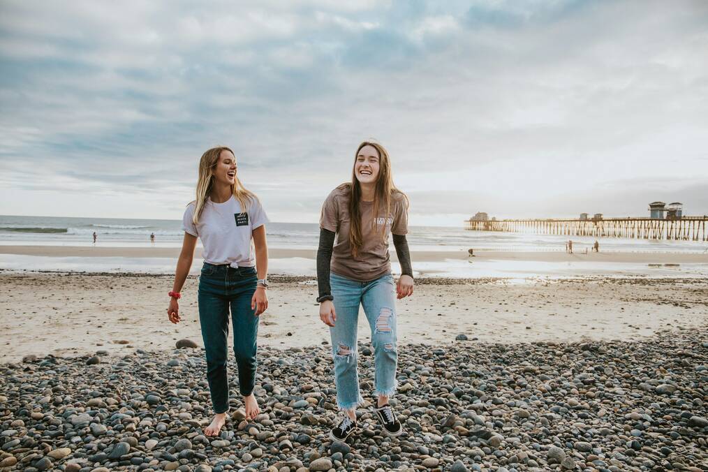 Two women walk on a rocky beach.