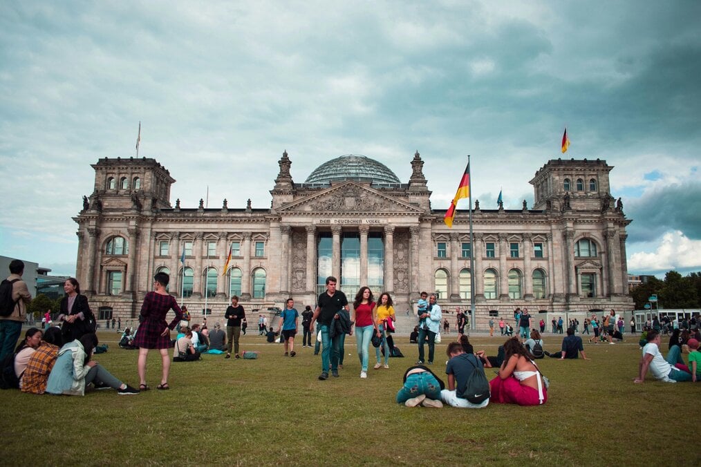 Photo by Federico Orlandi People sit on the grass in front of a building in Germany.