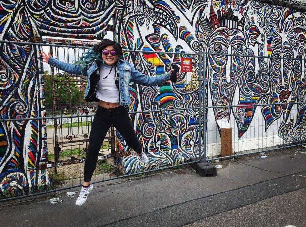 A woman jumps in the air in front of a painted mural.