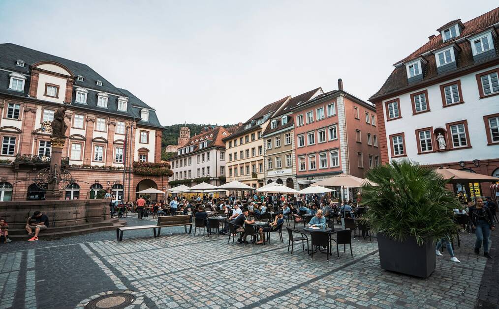 People sit outside at tables with umbrellas in a German square.