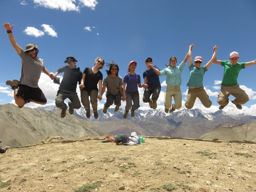 WTBD A group of teens jump in the air with mountains in the background.