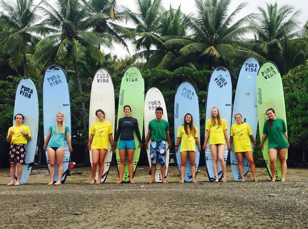 GW Teens stand on front of surf boards on the beach.
