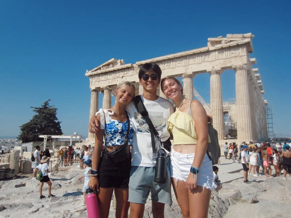TFT Three teens stand in front of ancient ruins in Italy.