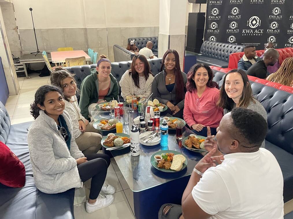 A group of people sit around a table with food and smile.