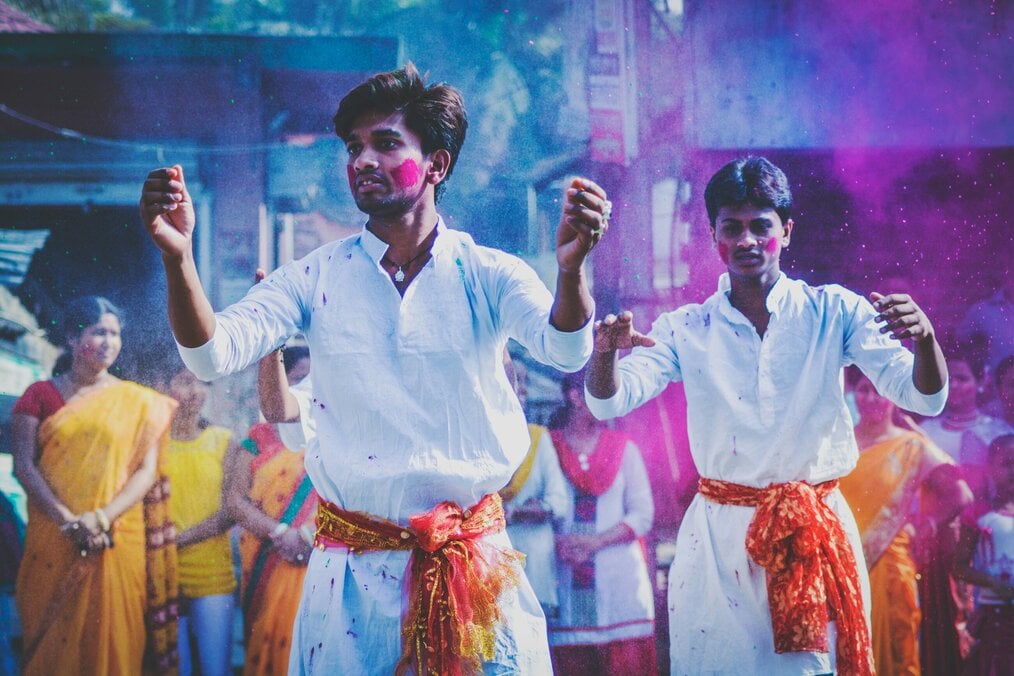 Two men dance with colored powder in the air.