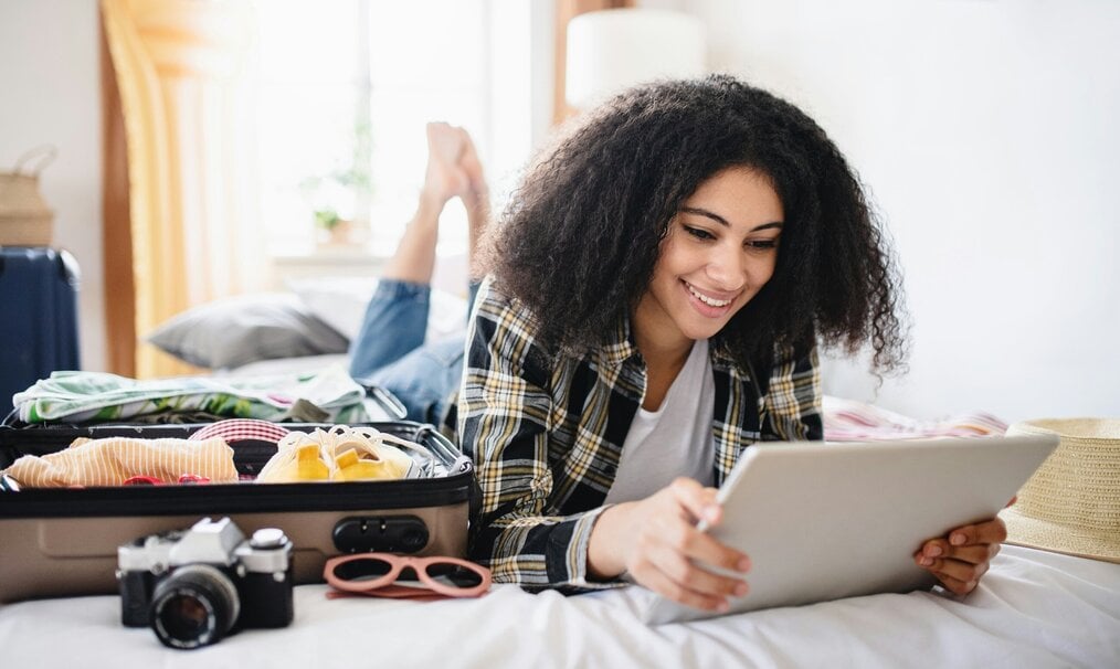 A woman looks at a tablet next to an open suitcase.