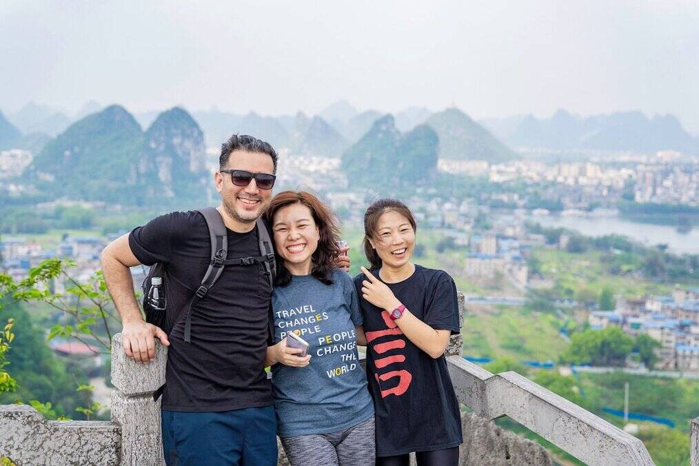 Three people pose with mountains in the background in China.