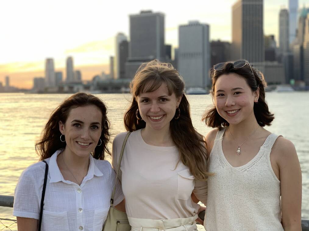 Three interns pose for a photo with a city skyline in the background.