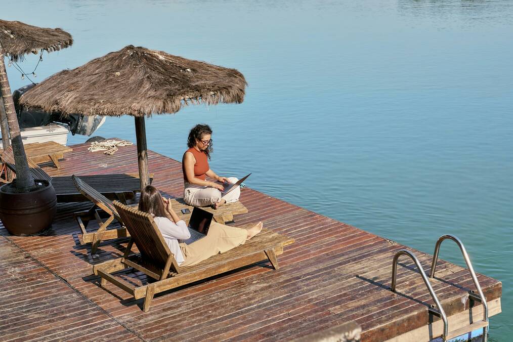Two people working on a laptop next to a lake