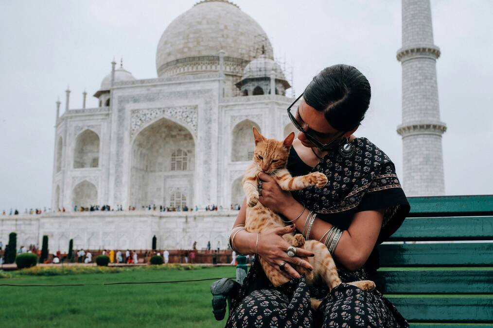 A woman holds a cat in front of the Taj Mahal.