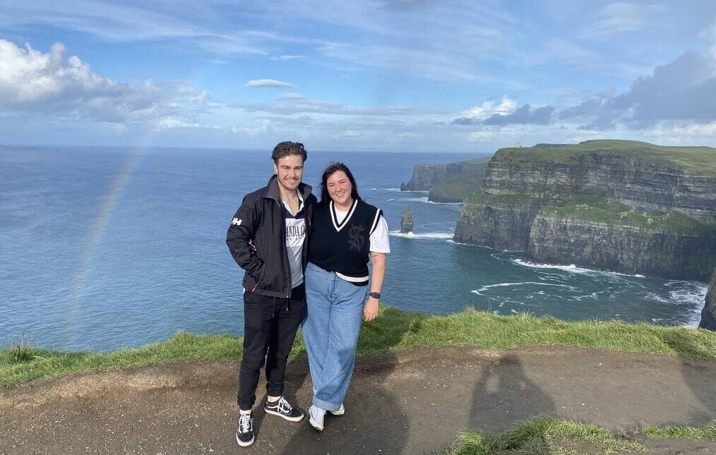 A man and a woman pose in front of cliffs in Ireland.
