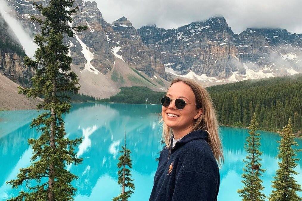 A woman smiles with a blue lake and mountains in the background.