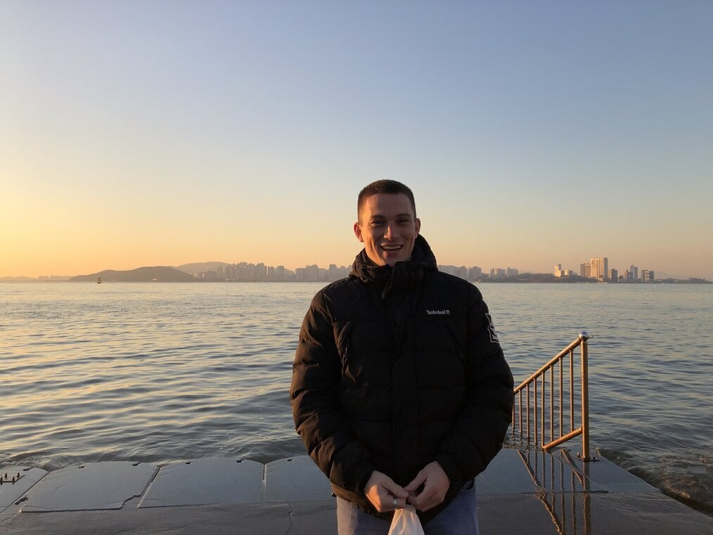 A man stands in front of a body of water at sunset.