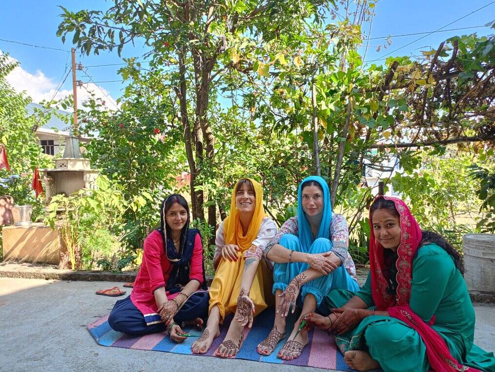 Four women sit and show off henna tattoos on arms.