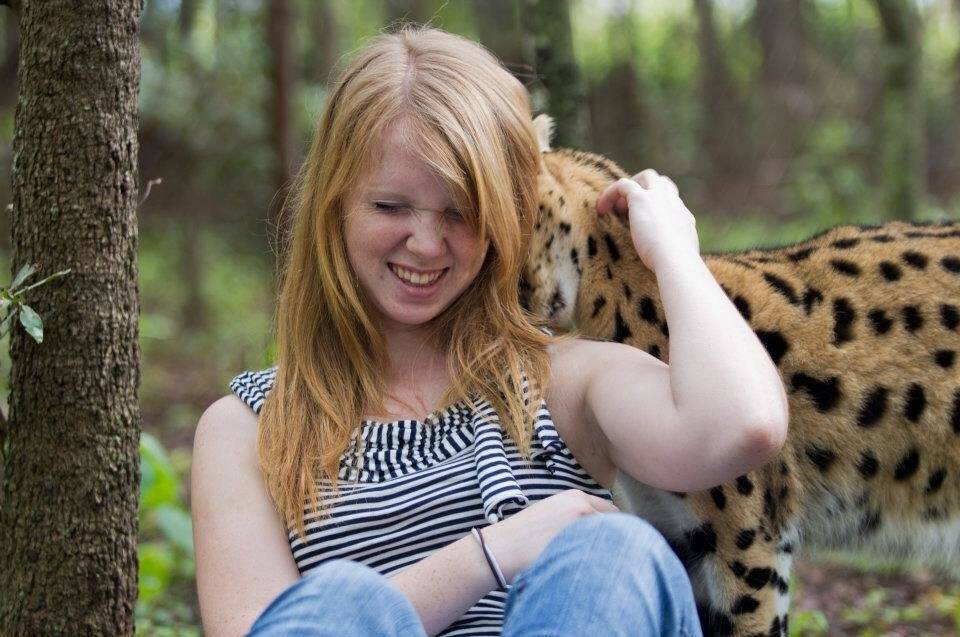A girl laughs as a leopard walks behind her.