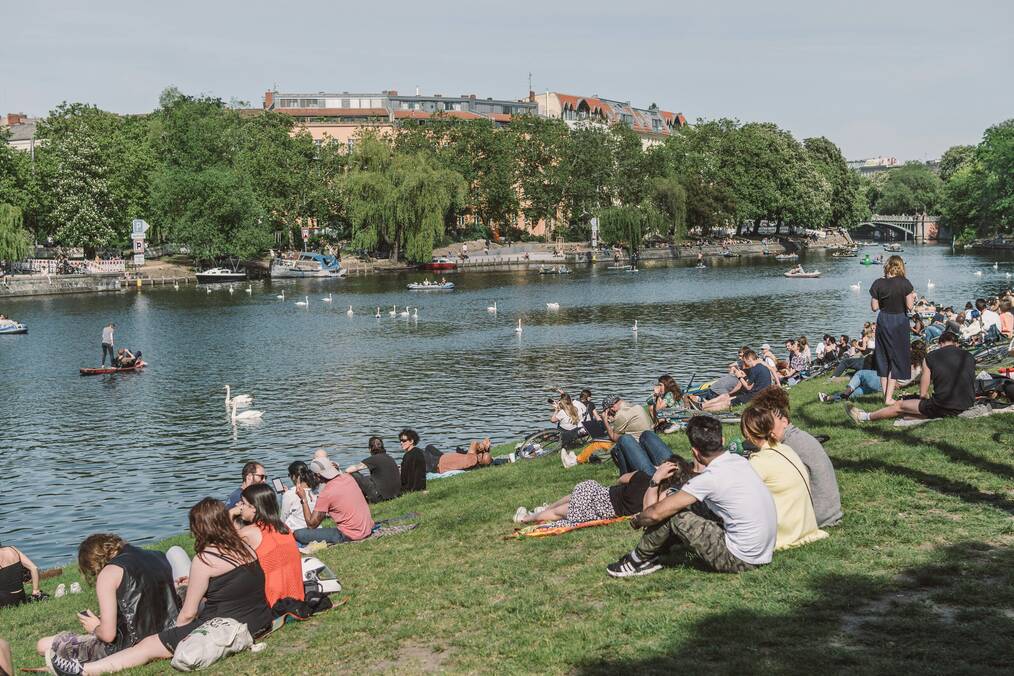 A large group of people sit on a hill near a river in Germany.