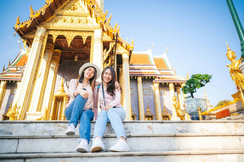 Two women sit in front of a golden temple in Cambodia.