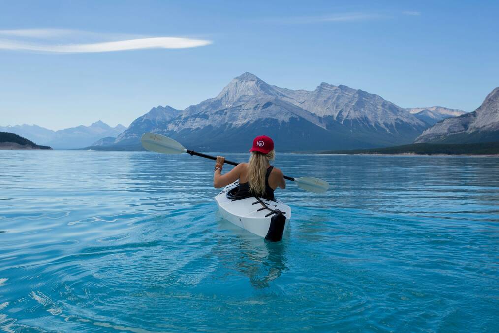 A woman paddles a canoe on clear blue water.