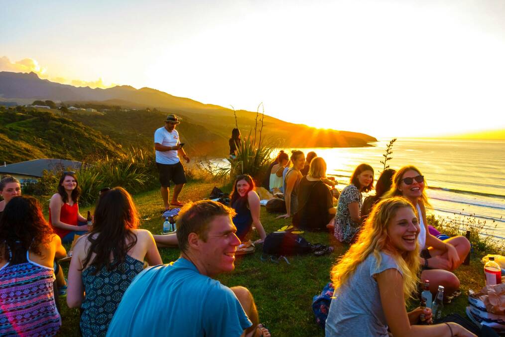 A group of people have a picnic near cliffs in NZ at sunset.