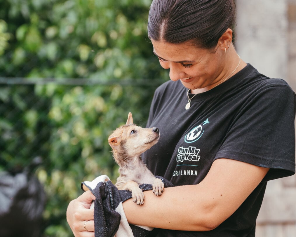 A woman holding a puppy looks at it and smiles.