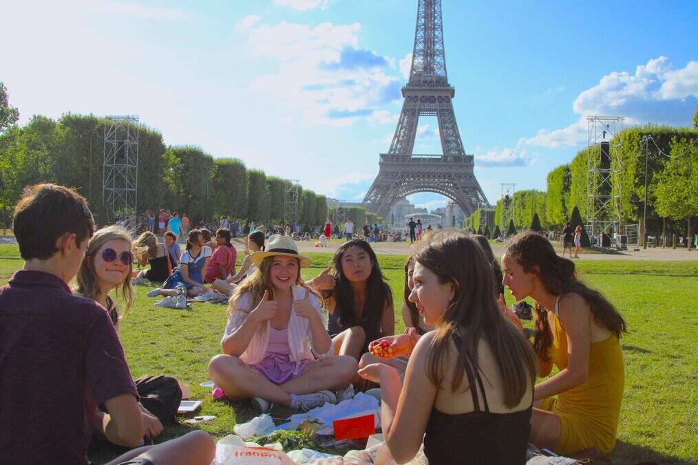 A group of teens have a picnic in front of the Eiffel Tower.