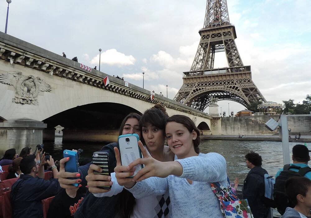 Three girls pose for selfies with the Eiffel Tower in the background.