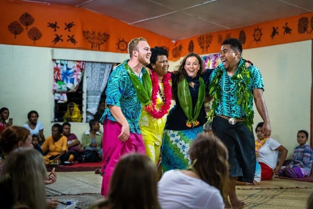 Four people with their arms around each other laugh and smile.