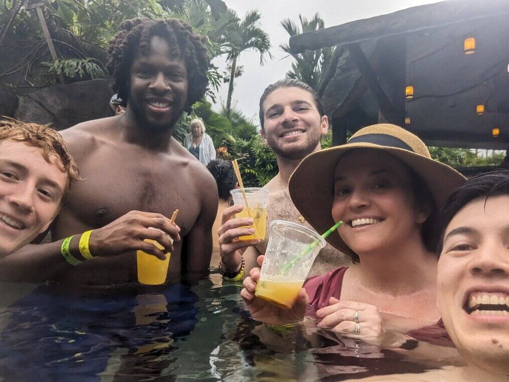 A group of volunteers pose in a hot spring while holding drinks.