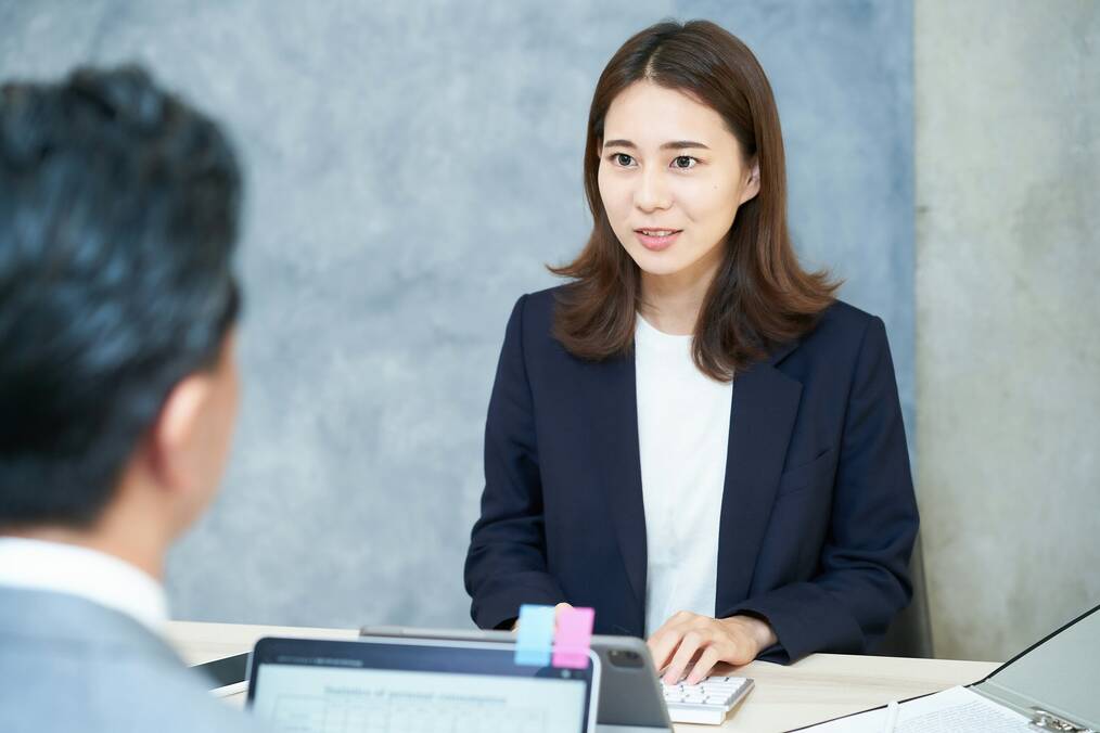 A woman wearing a black suit jacket smiles at her interviewer.