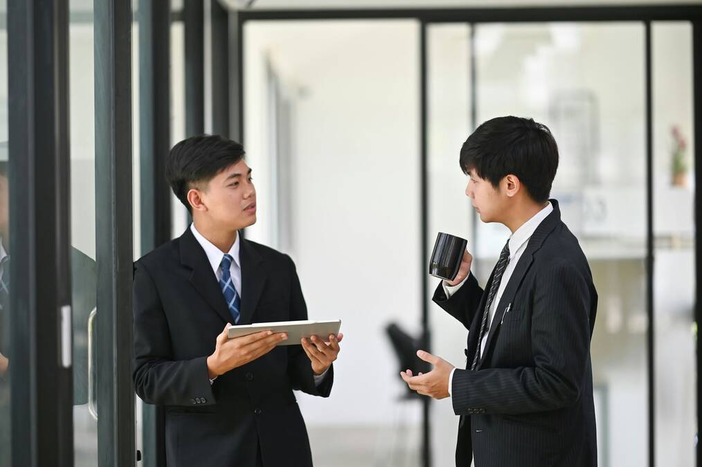 Two men stand and talk in an office.