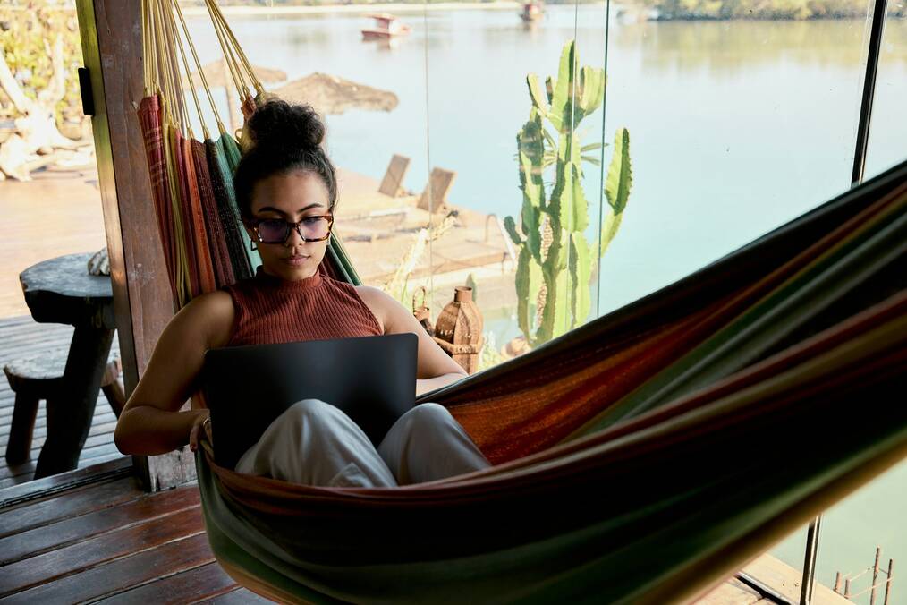 A woman working on a laptop sits in a hammock.