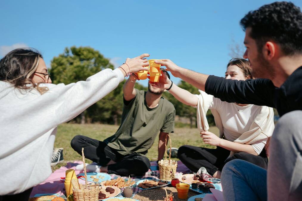 Four friends having a picnic toast their plastic cups.