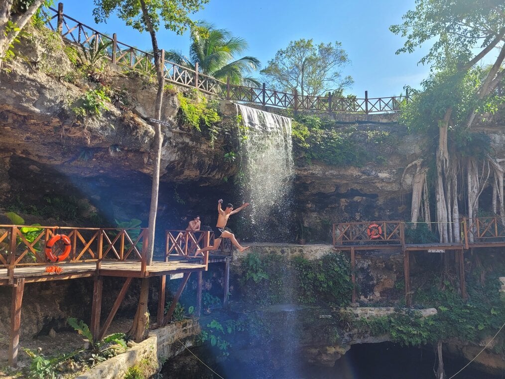 Cenote A man jumps off a platform into a body of water.